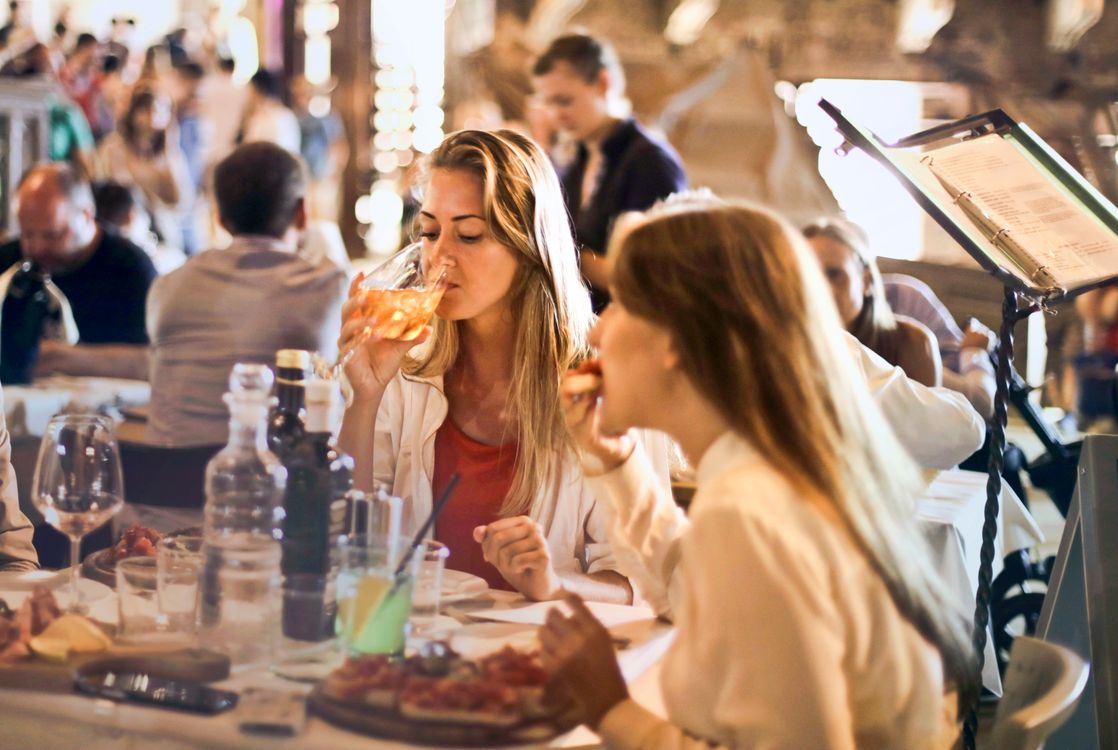 קבוצת חברים יושבת סביב שולחן במסעדה תוססת ומשלבת ארוחה משותפת כתחנה הראשונה במסלול הערב