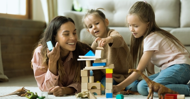 אמא משחקת עם הילדים שלה עם צעצועים על הרצפה