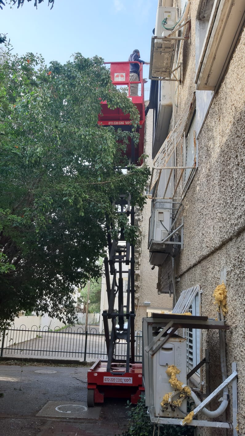 במת הרמה אדומה ניצבת ליד עץ ובניין אפור, ועליה עומד איש.